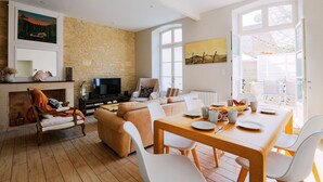 Una sala de estar moderna con pared de piedra, chimenea, sofá, mesa de comedor con sillas y televisor.