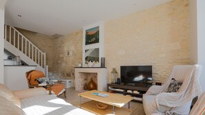 Una sala de estar con sofá, sillón, mesa de centro, televisión, chimenea y pared de piedra.