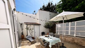 Un patio al aire libre con una mesa lista para comer, una silla, un sillón colgante y un paraguas grande.