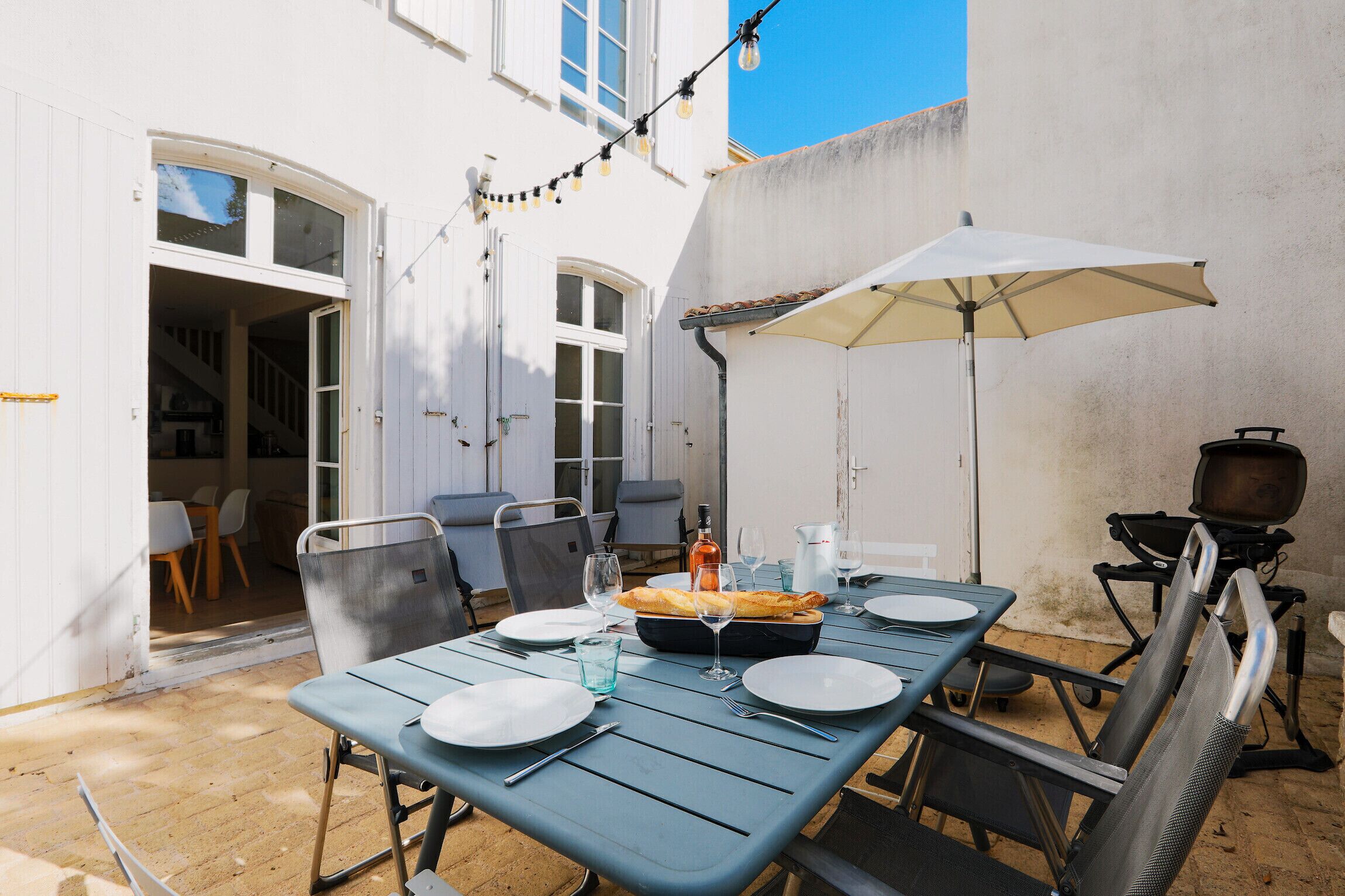 A patio with a table set for dining, outdoor seating, and a barbecue grill.
