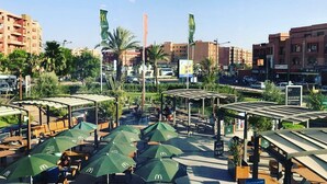 Zona all'aperto con sedute, ombrelloni verdi, palme e vista sullo skyline urbano.