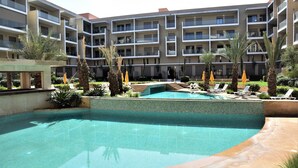 Un hotel moderno con piscina, lettini e palme.