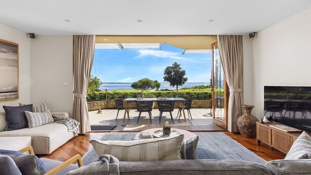 Ein geräumiges Wohnzimmer mit einer großen Schiebeglasdoor, die auf eine Terrasse im Freien führt. Das Zimmer verfügt über ein bequemes Sofa, einen Couchtisch und einen Fernseher auf einem Holzboden.