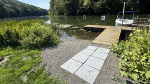 A wooden dock extending into a calm lake, surrounded by lush greenery and a clear sky. - Riverhouse NEW renovation, riverfront, game rm, fishing, swimming, paddle sports (Milford)