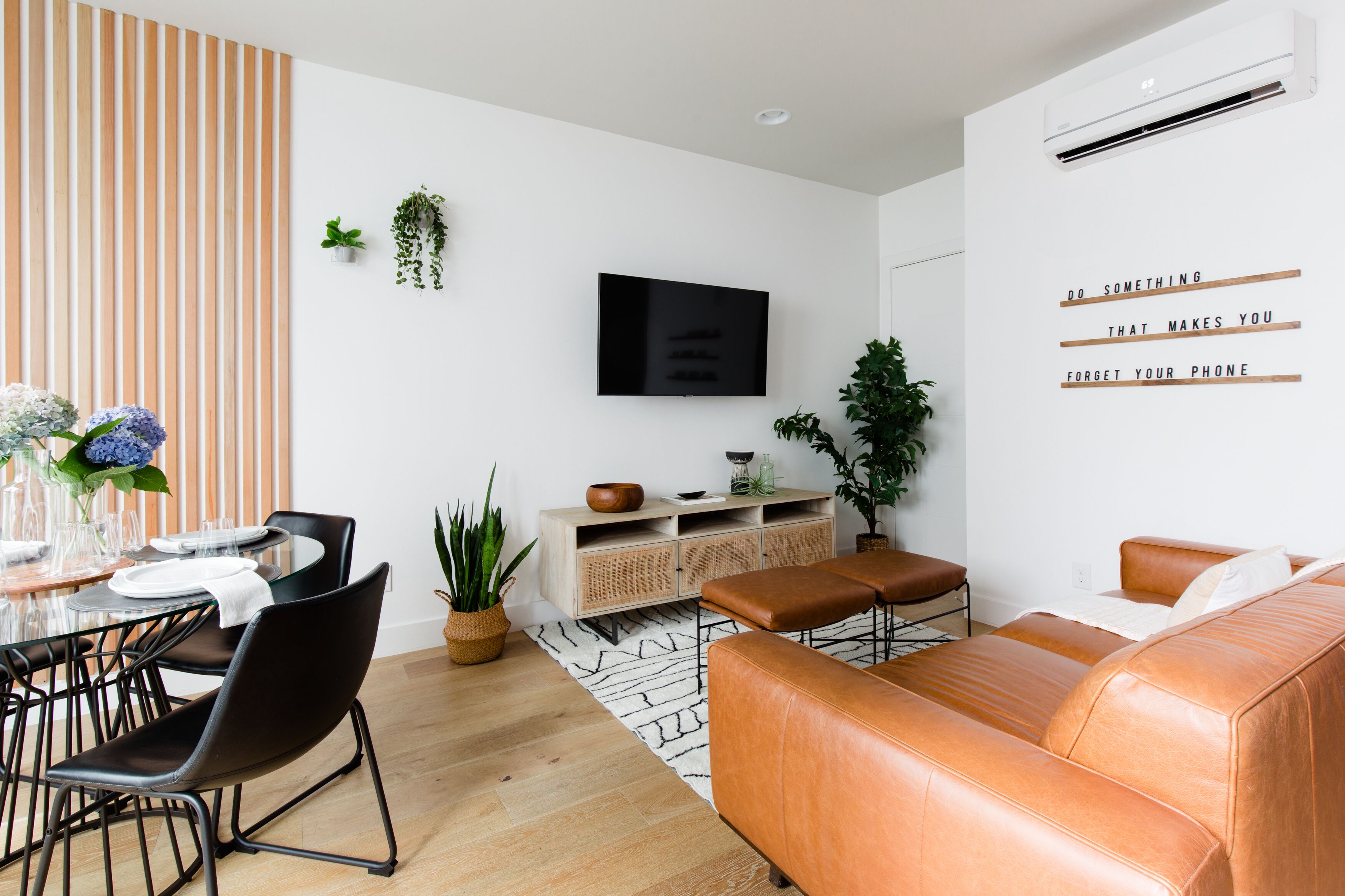 A modern living room with a TV, a sofa, a dining table with chairs, and a potted plant.