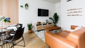 Un saló modern amb televisió, un sofà, una taula de menjador amb cadires i una planta en test.