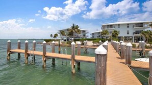 A wooden pier extending into calm waters, leading to a beachfront property with multiple balconies and palm trees. - Changes in Latitude (MARATHON)