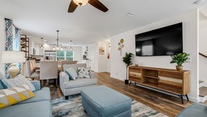 Een moderne woonkamer met een bank, poef, tv-meubel van hout en een plafondventilator.