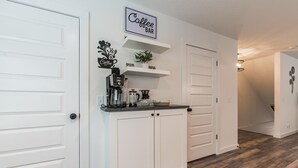 Een keuken met witte kastjes, een bord met daarop 'Coffee Bar', een koffieapparaat en een plantje op het aanrecht.