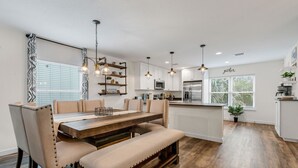Een moderne keuken met houten vloeren, een eethoek met een bank, hanglampen en uitzicht op de omgeving.