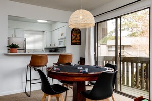 Un espace repas comprenant une table de poker, des chaises, un luminaire suspendu et une vue sur l’extérieur grâce à de grandes fenêtres.