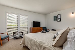 Une chambre à coucher comprenant un lit, une chaise, une commode, un téléviseur et une fenêtre avec des stores.