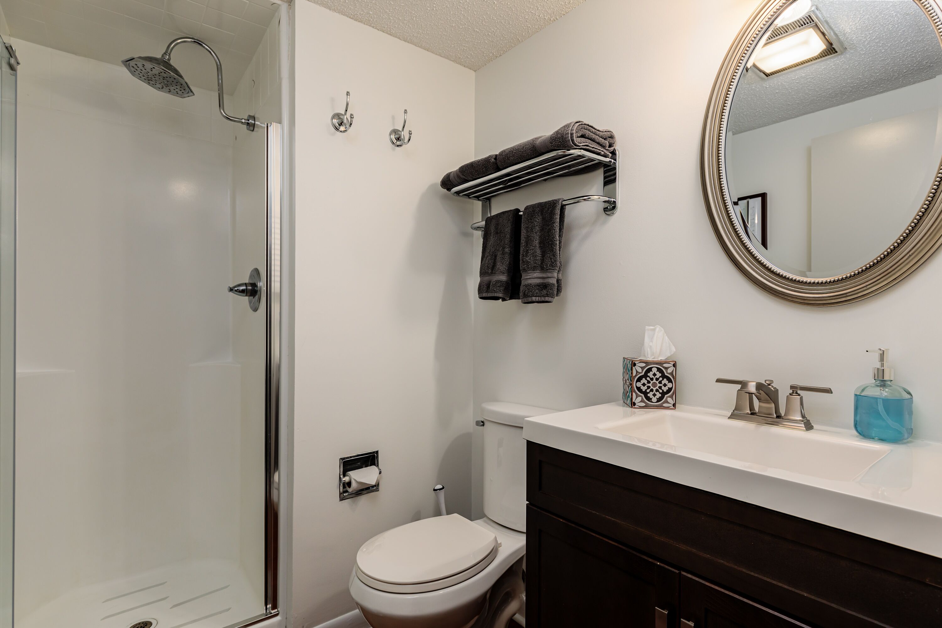 A bathroom with a shower, toilet, sink, and a large mirror.
