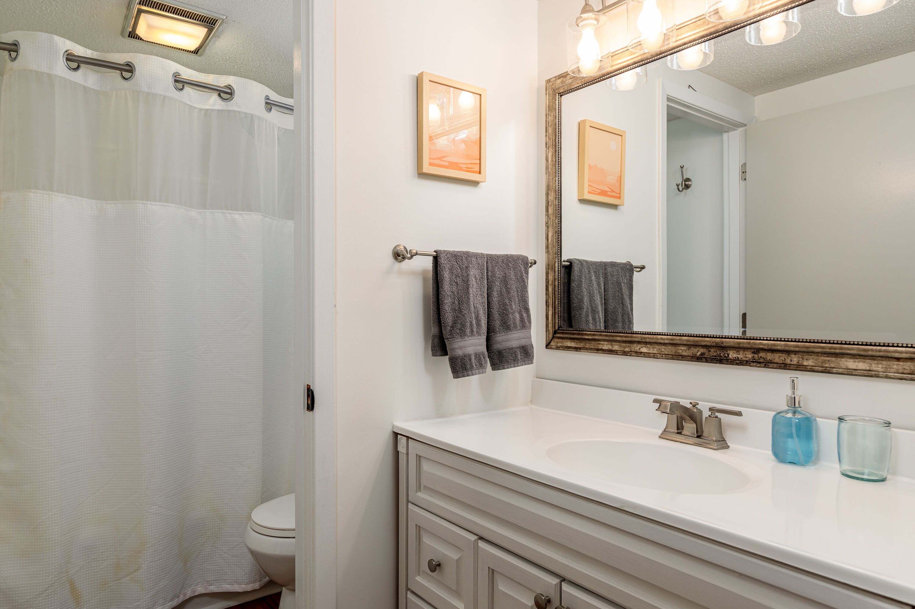 Une salle de bain avec un lavabo blanc, un miroir avec éclairage intégré et un rideau de douche.