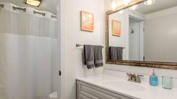 Une salle de bain avec un lavabo blanc, un miroir avec éclairage intégré et un rideau de douche.