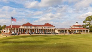 Een groot gebouw met een rood dak en meerdere kolommen, omgeven door een verzorgd gazon en een golfbaan.