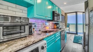 Een keuken met blauwgroene kastjes, een roestvrijstalen fornuis en een groot raam met uitzicht op een balkon.