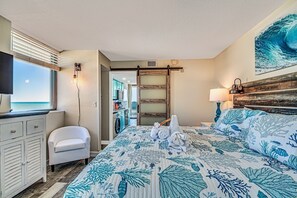 Een slaapkamer met een bed, een stoel, een televisie en uitzicht op de oceaan.