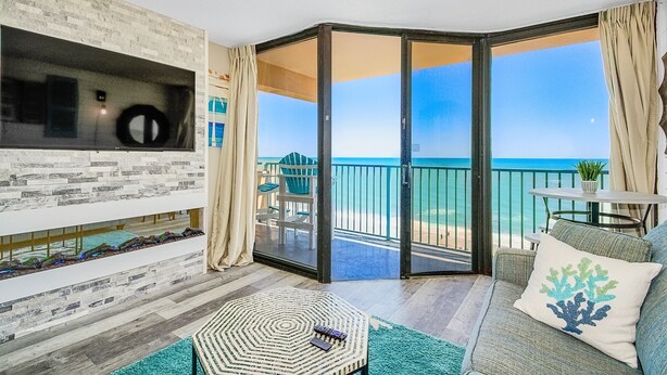 Een moderne woonkamer met een grote schuifglazen deur die uitkomt op een balkon met uitzicht op het strand.