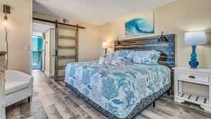 Een slaapkamer met een bed, nachtkastjes, een stoel en een deur naar een andere kamer.