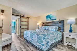 Un dormitorio con cama, mesitas de noche, una silla y una puerta que da a otra habitación.