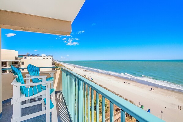 Enjoy the serene beach views from this balcony, featuring comfortable Adirondack chairs and a table.