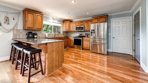 A modern kitchen with wooden cabinets, stainless steel appliances, and a bar area with stools. - Double Down: Spacious Lakefront Retreat with Stunning Views & Hot Tub (Bella Vista)