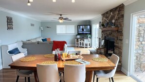 A dining area with a wooden table, four chairs, and a television in the background. - Double Down: Spacious Lakefront Retreat with Stunning Views & Hot Tub (Bella Vista)