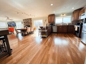 A spacious kitchen with wooden flooring, a dining area with a table and chairs, a built-in oven, and a stone fireplace.