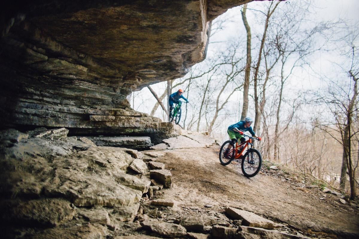 A mountain biker on a rocky trail with a large rock formation overhead.