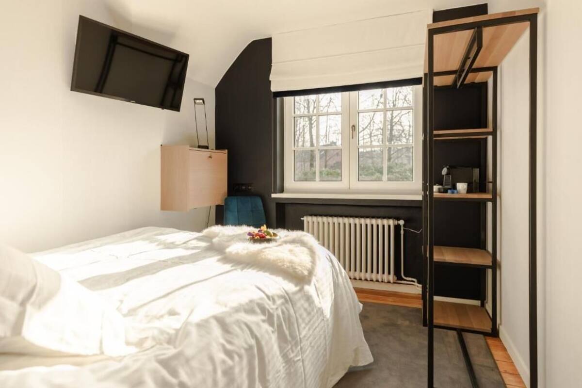 A bedroom with a bed, a TV mounted on the wall, a window with a view, and a built-in shelf unit.