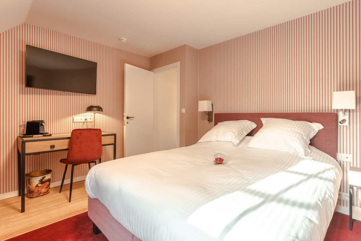 A hotel room with a bed, a desk, a chair, a television, and a lamp.
