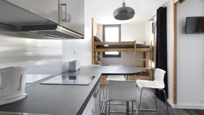 Une cuisine compacte avec un îlot central, un lit superposé et un coin repas.