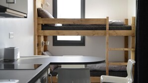 Une petite pièce comprenant un lit superposé, une petite table et une chaise.