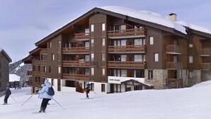 Un bâtiment en bois à plusieurs étages, doté de balcons, portant l’inscription « AIGUE MARINE », dans un décor enneigé.