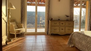 Een slaapkamer met een bed, een dressoir, een stoel en een balkon met uitzicht op het landschap.