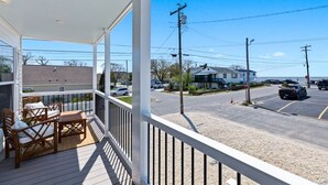 Un espacio al aire libre techado con una mesa y sillas, vista a una calle con coches aparcados y un edificio al fondo.