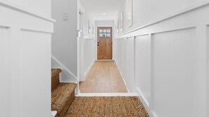 Un pasillo estrecho con paredes blancas, suelo de madera y una puerta de madera al final.