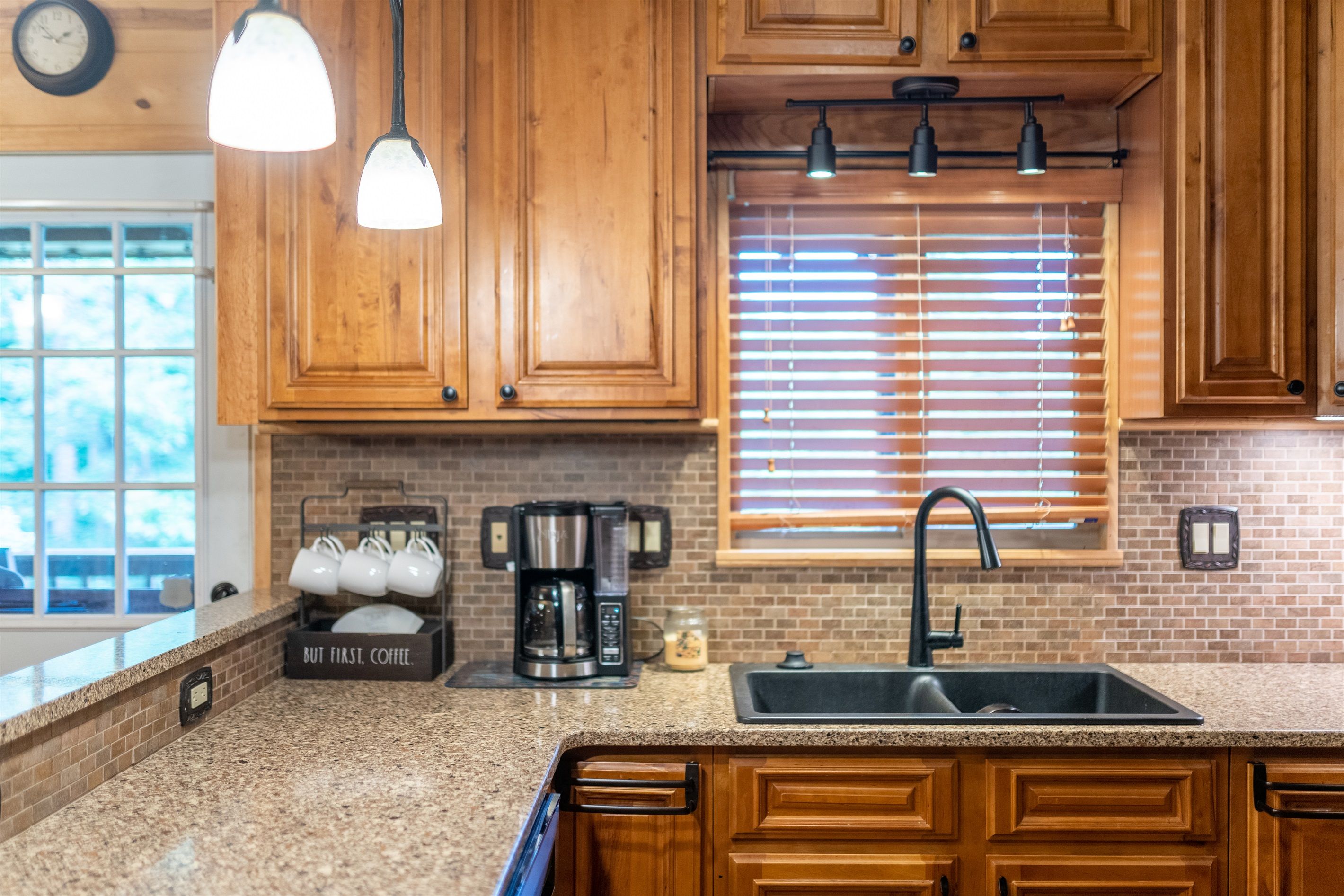 A kitchen with wooden cabinets, a coffee maker, a sink, and a window with blinds.