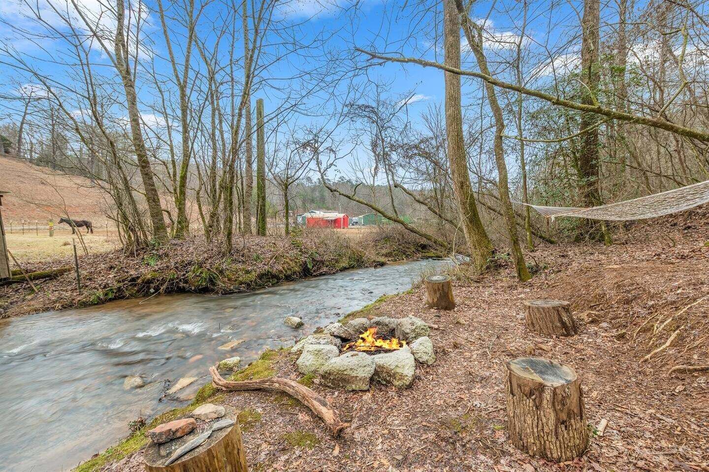 A river with a campfire, surrounded by trees and a hammock.