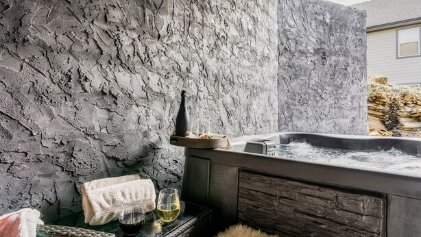 A spa area with a stone wall, a hot tub, towels, and a wicker basket. - Paws Retreat: 5BR/3BA, Pvt Hot Tub - Sleeps 14 (sevierville)
