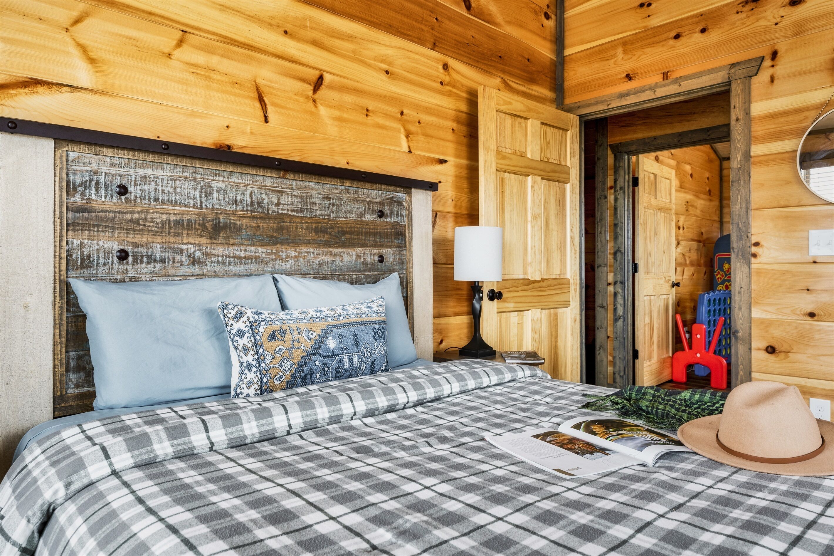 Una habitación de cabaña de madera con una cama, almohadas, una lámpara y un sombrero sobre la cama.