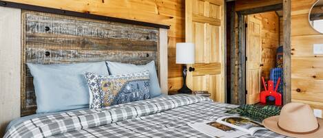 Una habitación de cabaña de madera con una cama, almohadas, una lámpara y un sombrero sobre la cama.