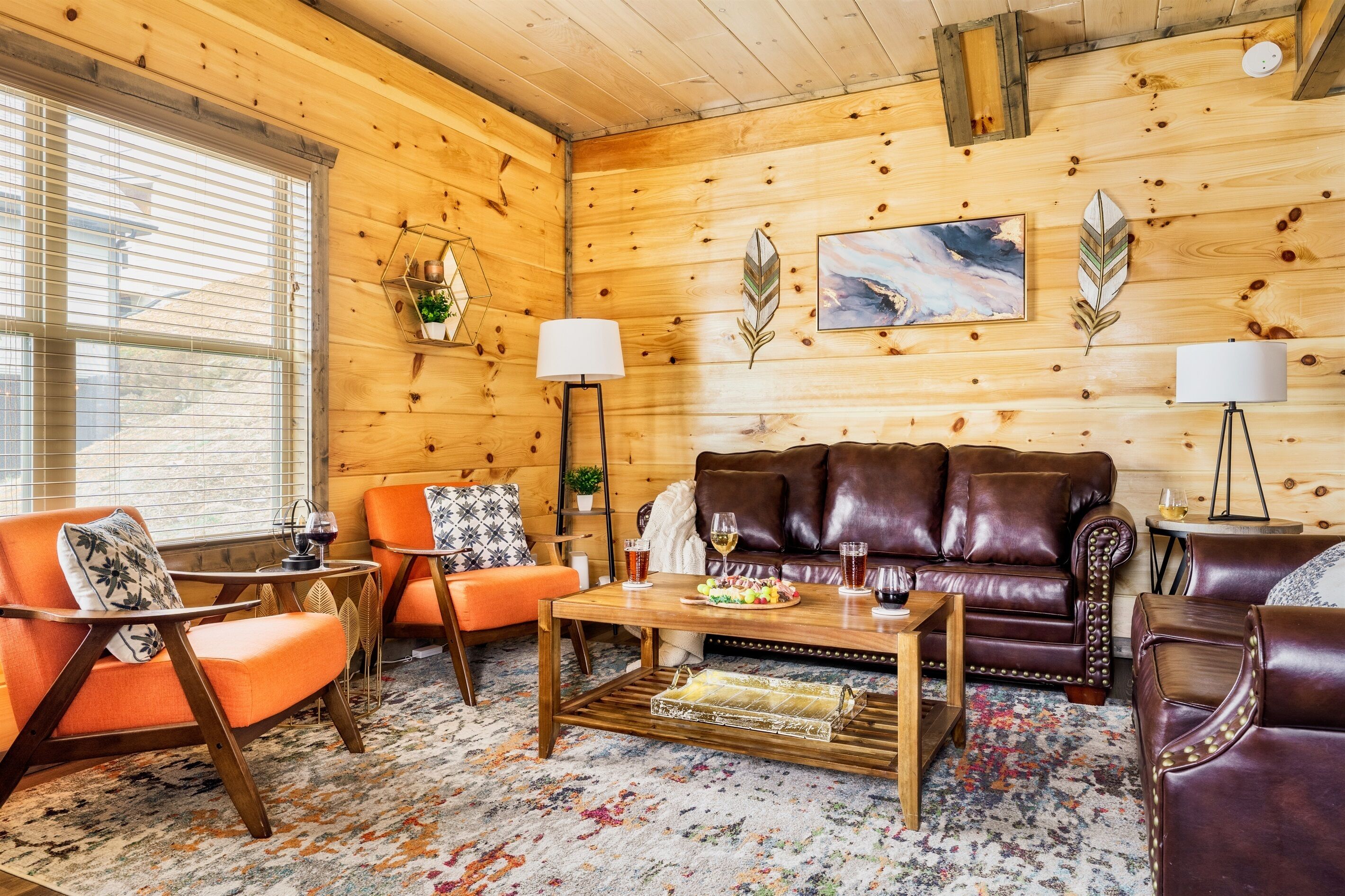 Een gezellige woonkamer met een bruine leren bank, oranje fauteuils en een houten salontafel.