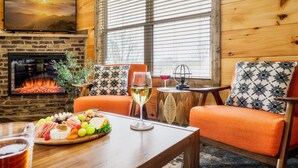 A cozy room with a stone fireplace, a television mounted above it, and a large window with blinds. - Paws Retreat: 5BR/3BA, Pvt Hot Tub - Sleeps 14 (sevierville)