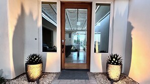 A modern entrance with a wooden door, two potted plants, and a glass door leading to a living area.