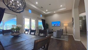 A spacious living area with a wooden dining table, comfortable seating, a flat-screen TV, and a view of the outdoors.