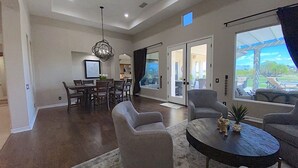A spacious living room with a dining area, a large window with a view, and a modern chandelier.