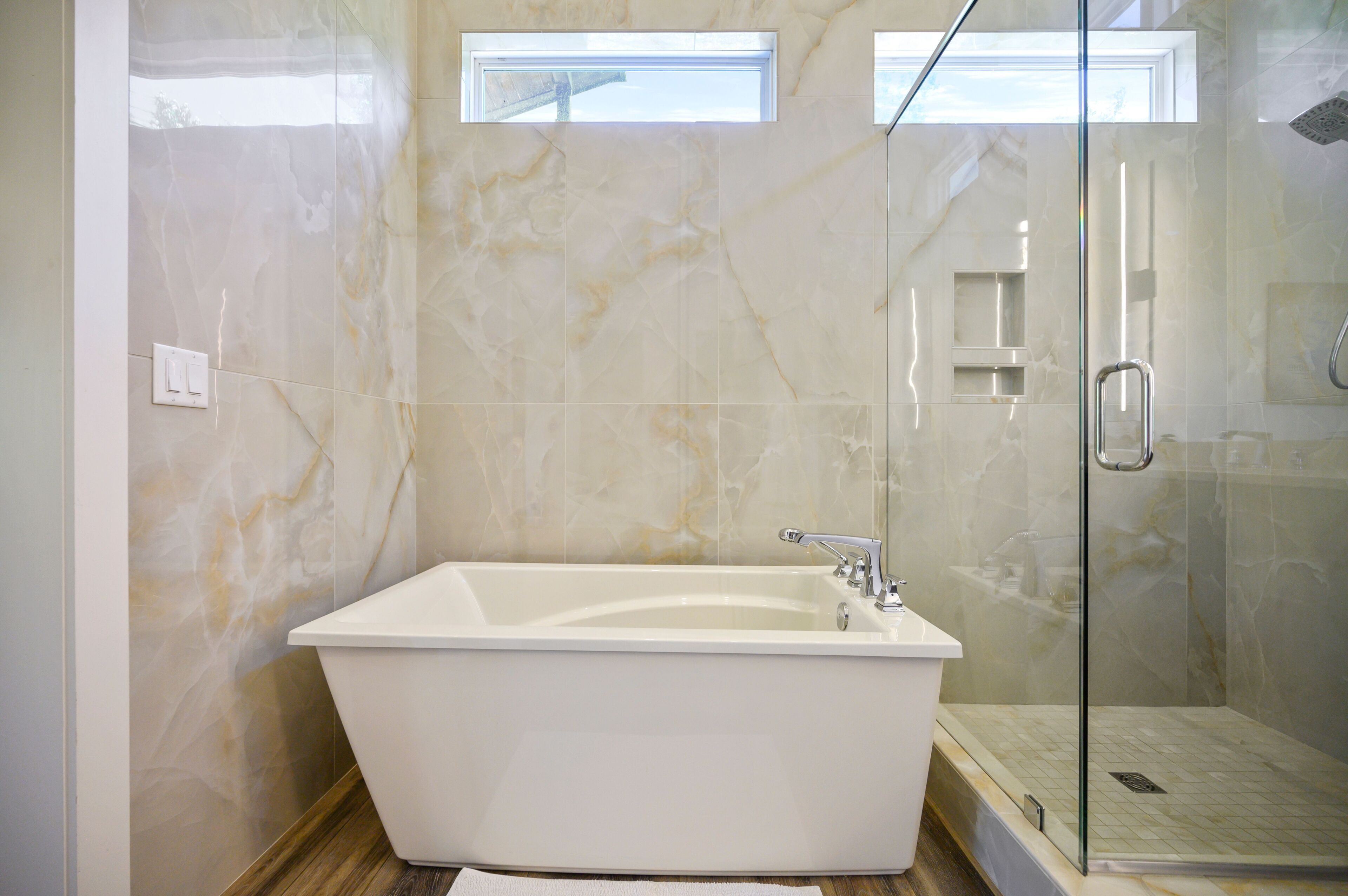 A modern bathroom with a freestanding bathtub, a glass-enclosed shower, and marble walls.