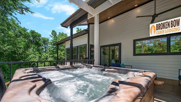 Un jacuzzi en una terraza de madera con vista a árboles. Un letrero dice 'Broken Bow Cabin Lodging'.